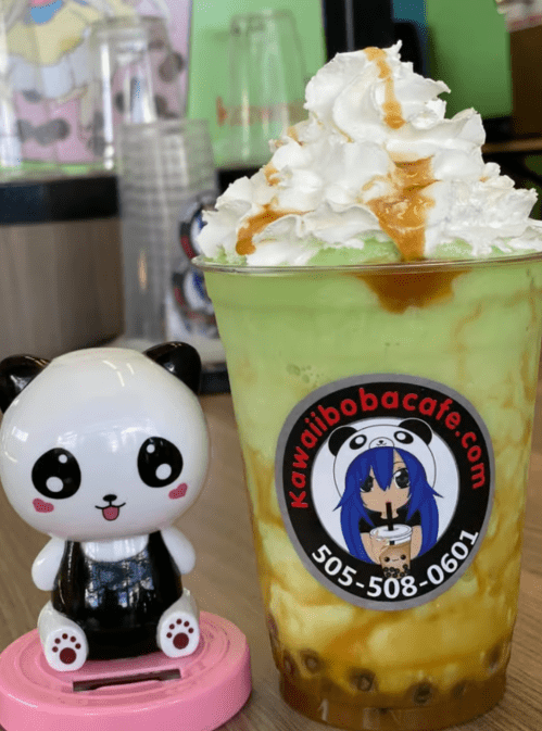 A green dessert drink topped with whipped cream and caramel, next to a cute panda figurine.